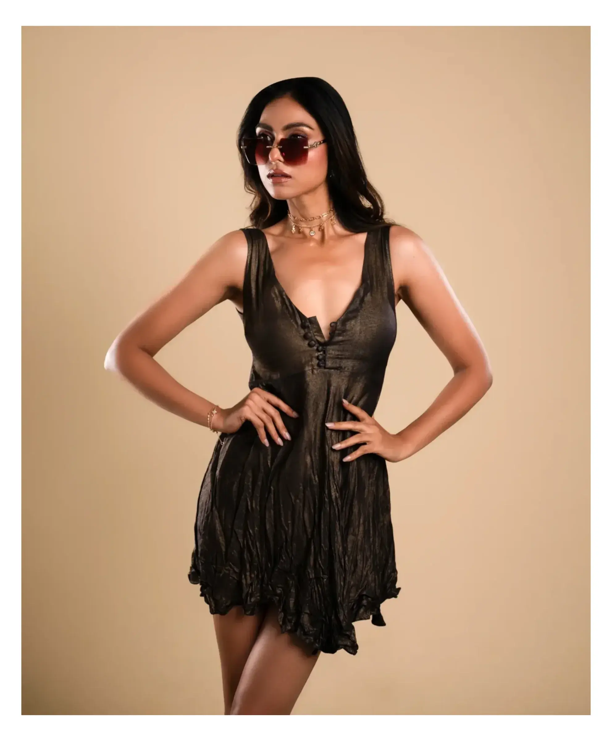 Model in a black dress and sunglasses against a warm studio backdrop
