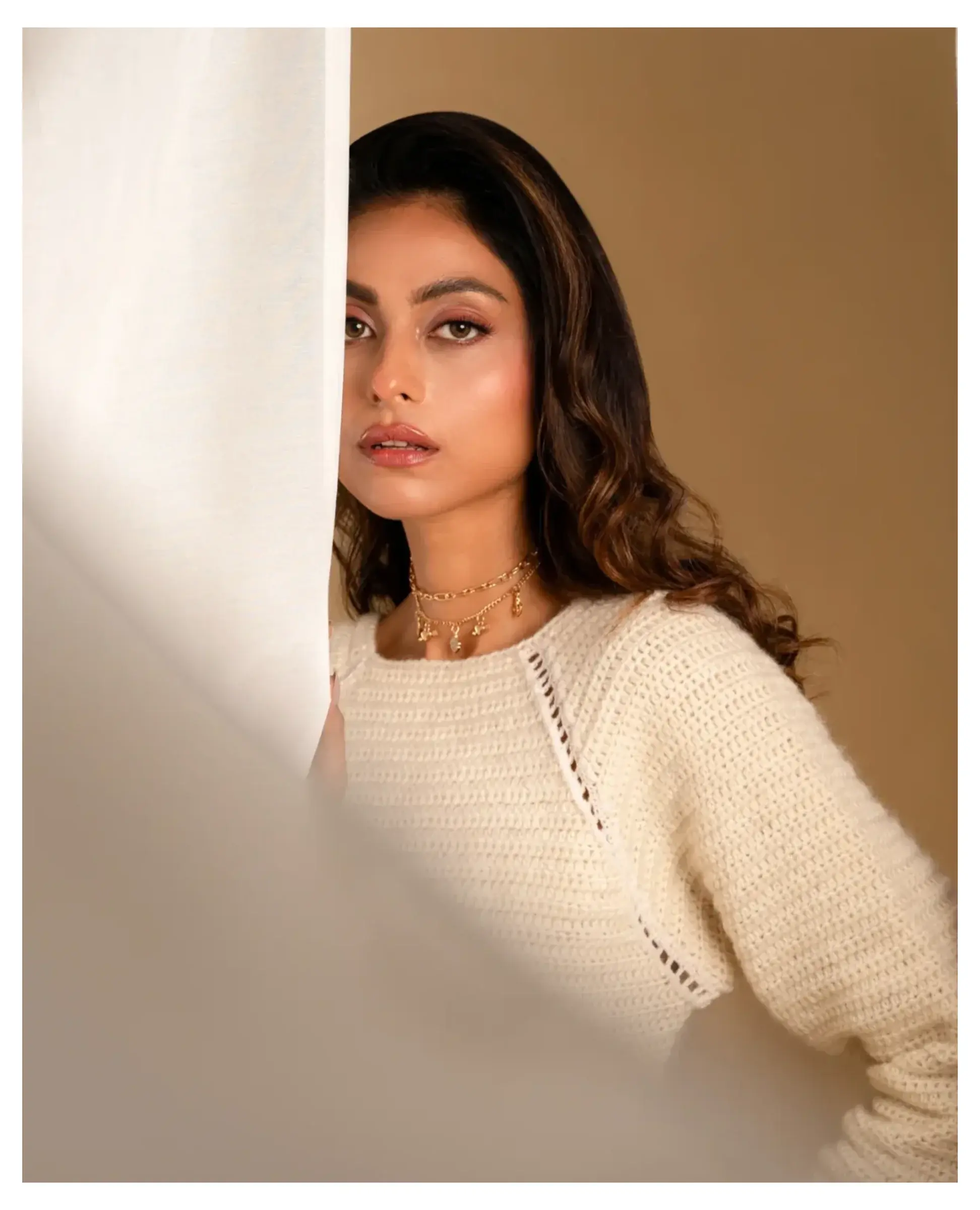 Soft portrait of a woman in a cream knit top, framed by fabric