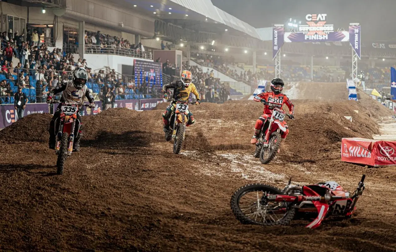 Supercross riders navigate a dirt corner in a floodlit stadium