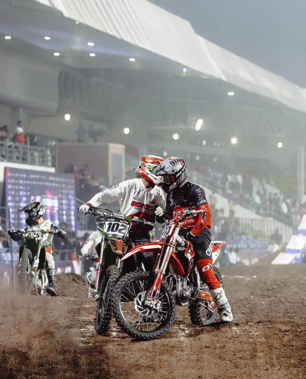 A motocross rider races across the dirt under spotlights